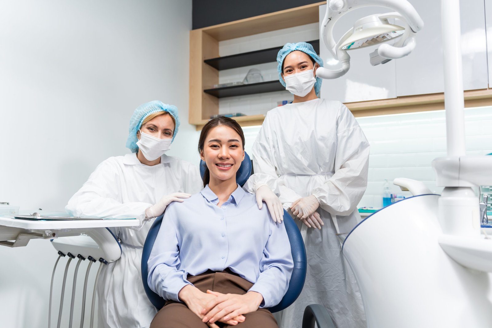 Portrait of Asian young woman patient and dentist workers in the clinic. Attractive girl sit on dental chair after getting dental treatment from doctor during appointment then smile, looking at camera