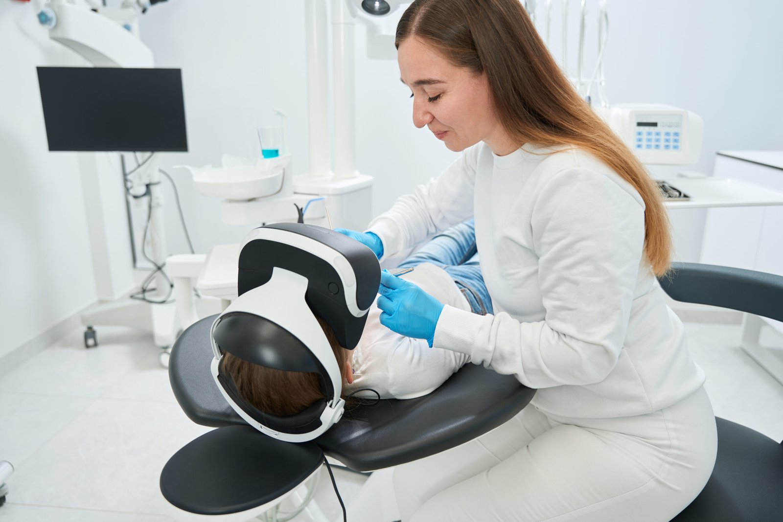 Concentrated pediatric dentist with diagnostic tools in hands leaning over patient in VR headset